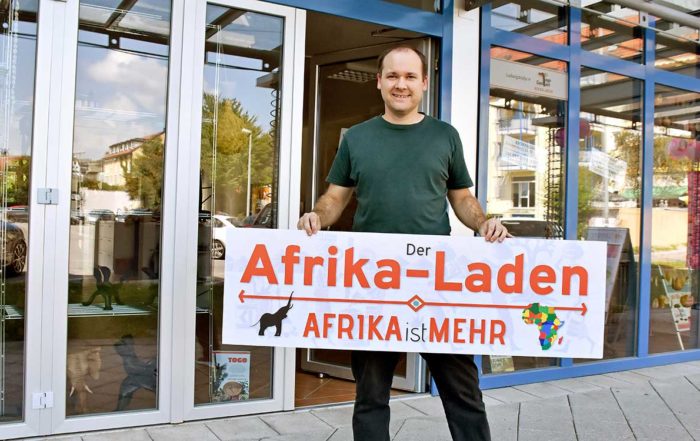 Andy Kopp hält das Schild des neuen Afrika-Ladens hoch
